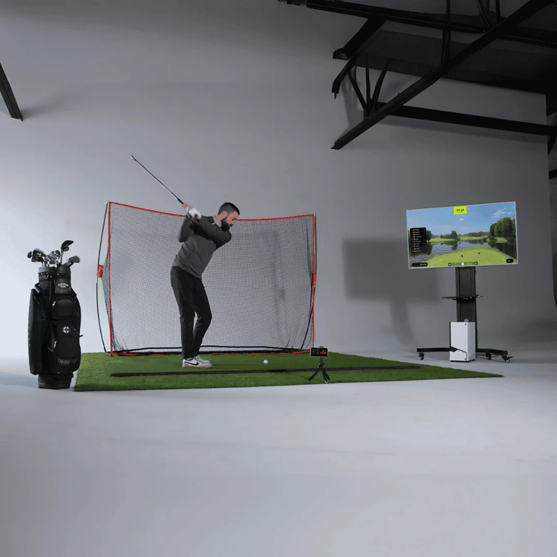 Red Stakes Golf Mobile Golf Starter Bundle indoor golf simulator man swinging club at net next to screen.